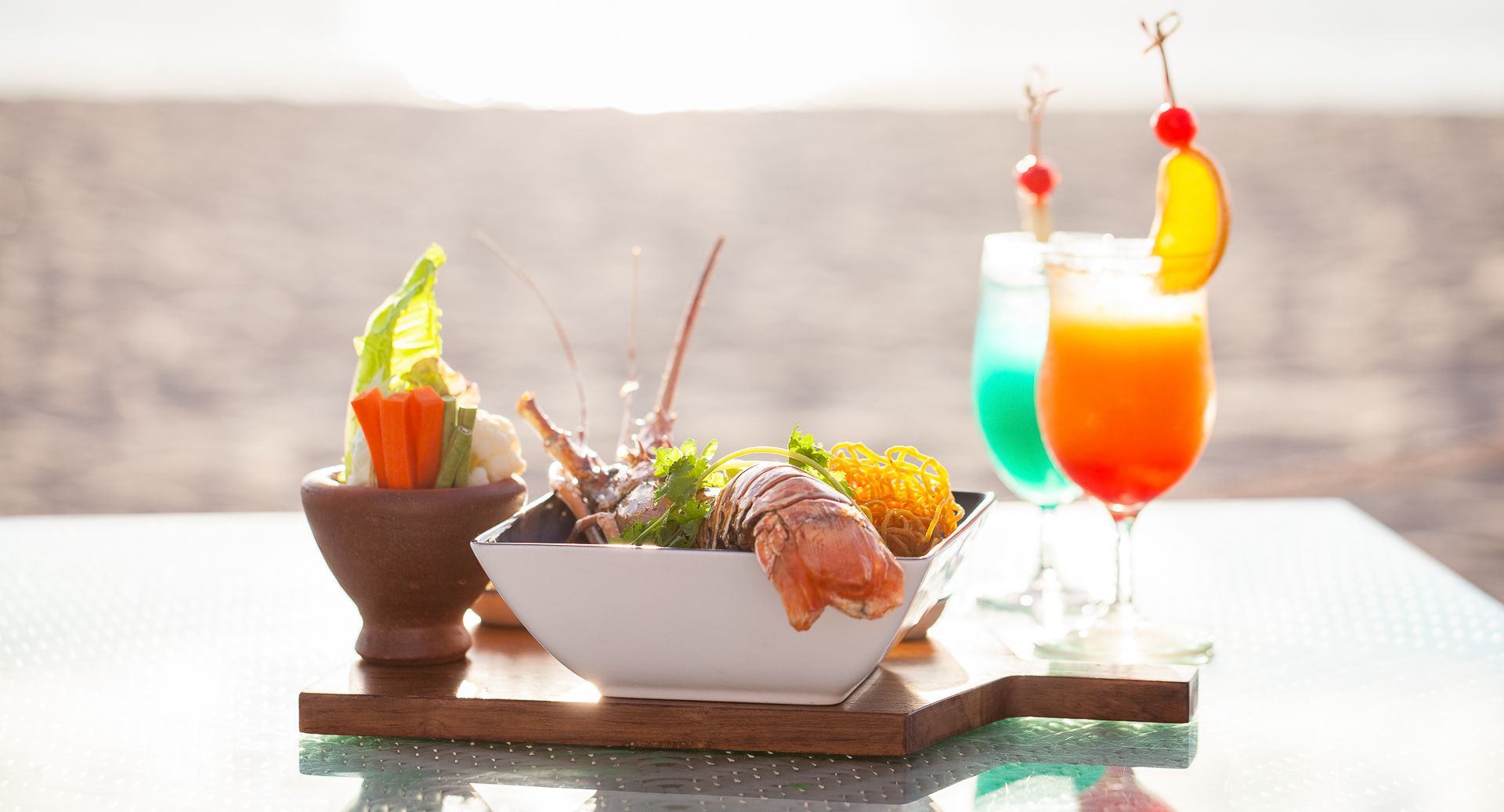A seaside appetizer spread: shrimp and veggie bowls with two colorful cocktails on a table.