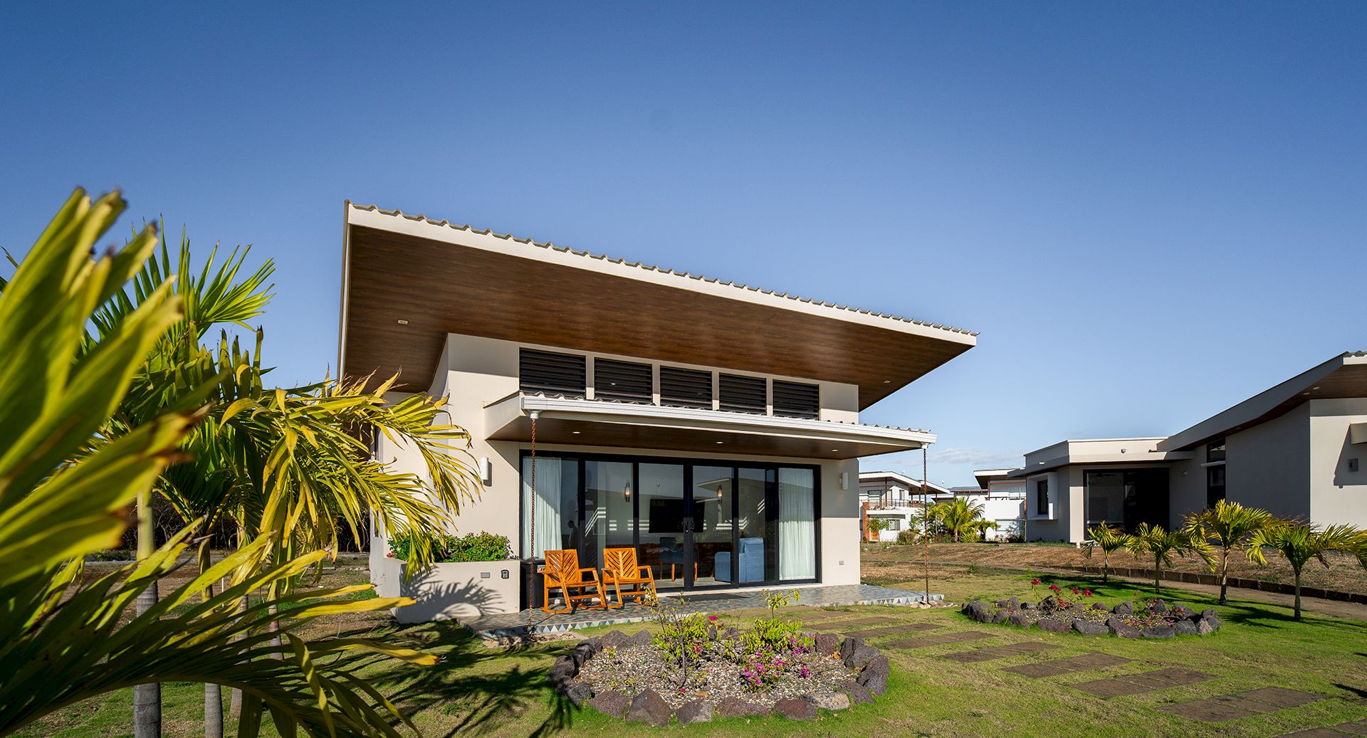 A modern home with palm plants, an outdoor patio, and a clear blue sky in the background.