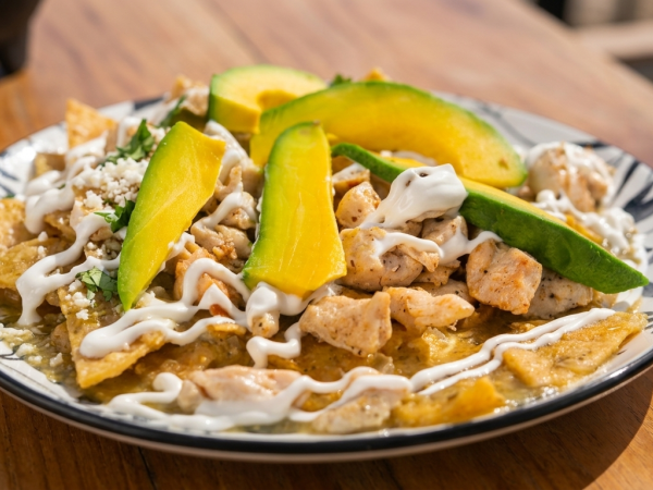 A plate of nachos topped with chicken, melted cheese, jalape&ntilde;os, mango, and a creamy drizzle.