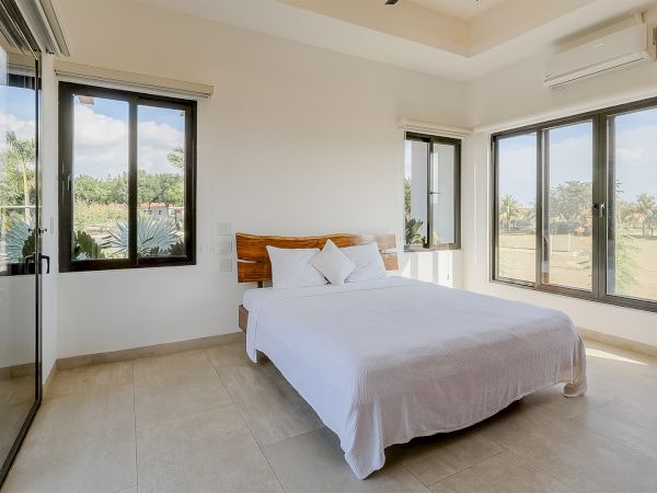 A bright modern bedroom with a white bed, large windows, and a wall-mounted air conditioner.