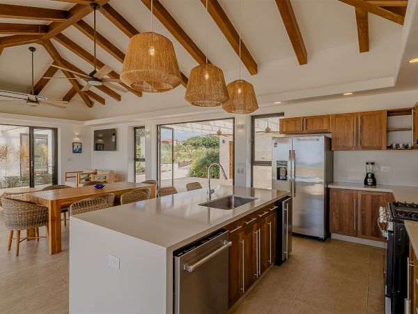 Open-plan kitchen with wood cabinets, a central island, stainless appliances, and hanging rattan lights above a dining area.