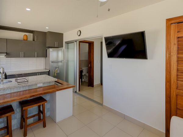Bright modern kitchen with granite island, stainless stove, gray cabinets, a wall TV, and tiled floor.