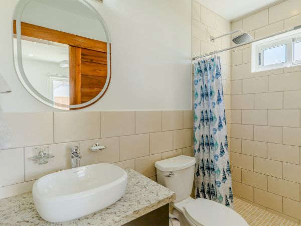 A modern bathroom with a round mirror, marble vanity sink, toilet, and a blue patterned shower curtain.