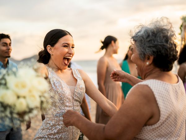 At a sunset beach party, a woman in a sparkly dress laughs and dances with friends.