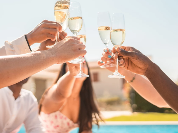 Friends clink champagne flutes poolside in the sun, toasting a celebration together.
