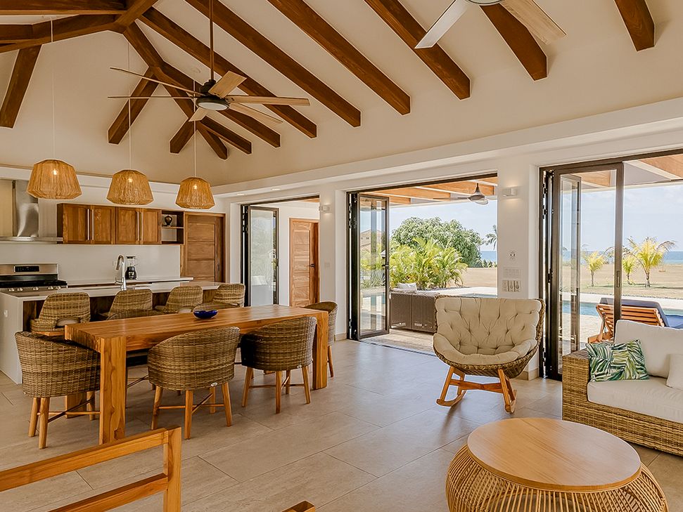 A bright modern open-plan living and kitchen area with wood ceilings, ceiling fans, wicker furniture, and large sliding glass doors.