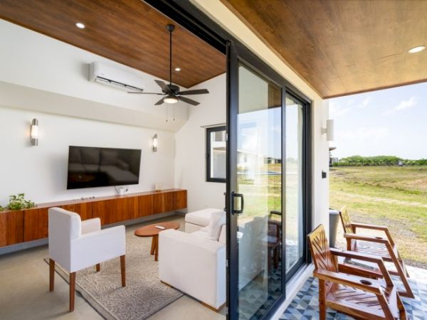 A modern living room with sofas, a wall TV, a ceiling fan, and sliding glass doors opening to an outdoor patio.