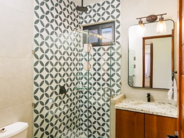 A modern bathroom with patterned tile shower, glass door, vanity sink and mirror with two wall lights above it.