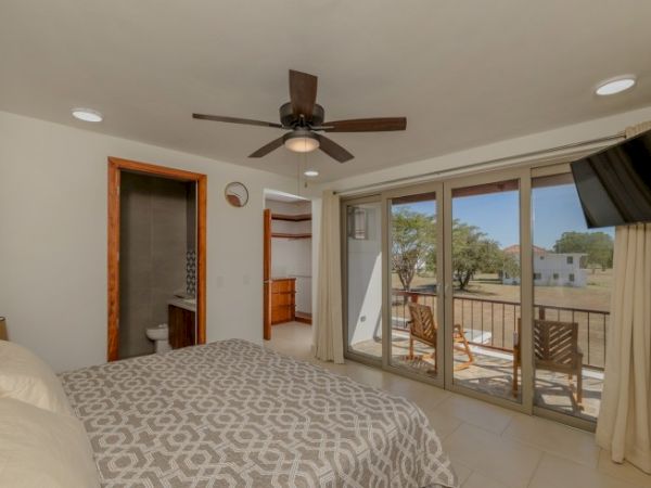 Bright bedroom with patterned bedspread, ceiling fan, en-suite bathroom door, and large sliding doors to a balcony.