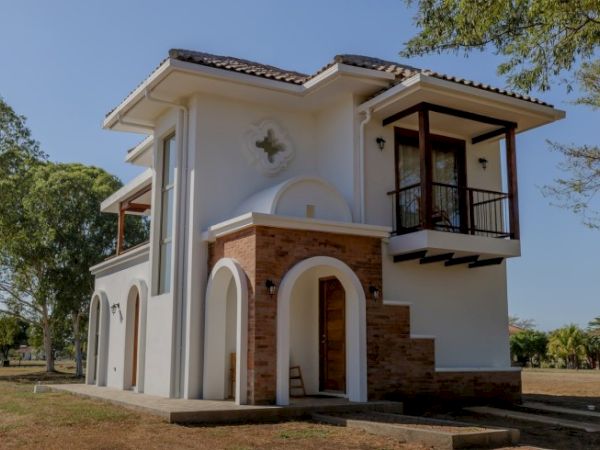 A modern white villa with arched entryways, brick accents, and a dark-wood balcony under a tiled roof.