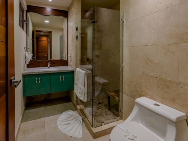 A modern bathroom with green vanity, glass shower, tiled walls, and a white toilet.