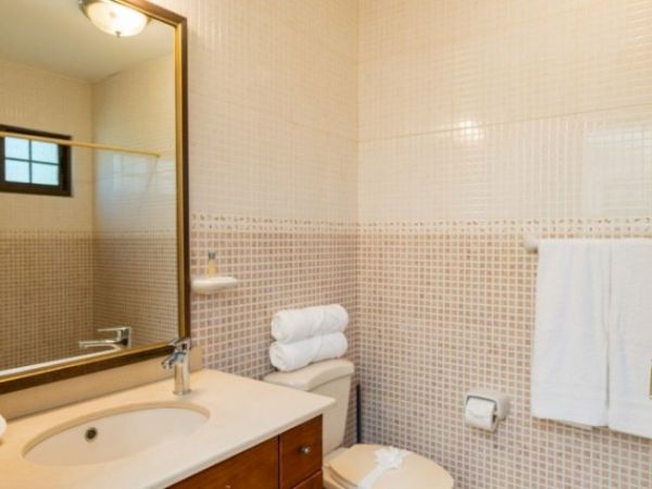 A small tiled bathroom with a vanity sink, mirror, toilet, and stacked white towels with shower curtains.