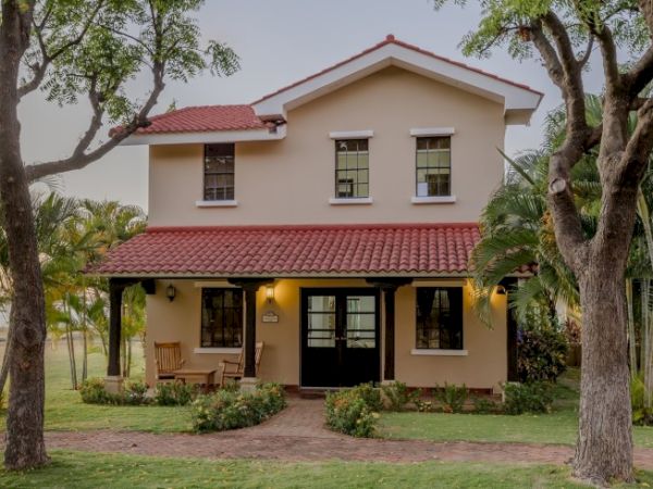 A white two-story house with a red tile roof, front porch, windows, and trees and lawn around it.