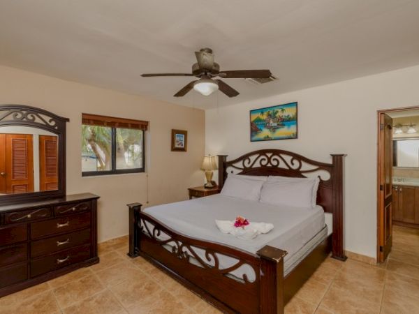 A spacious bedroom with a wooden bed, ceiling fan, dresser, and framed art on the walls.