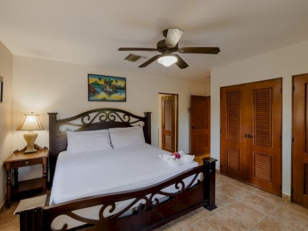 A tidy bedroom with a dark iron bed, lamp, ceiling fan, tiled floor, and wooden louvered doors.