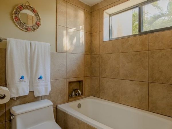 A tiled bathroom with a bathtub, toilet, two towels, and a round mirror decorated with flowers.