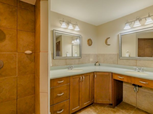 A bright bathroom with two double sinks, wood vanity cabinets, and matching light fixtures above mirrors.