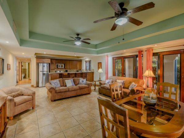 Spacious living room with beige sofas, dining table, kitchen in back, and two ceiling fans.