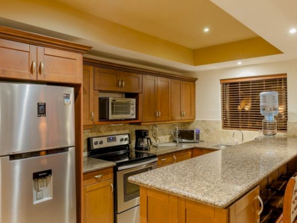 Modern kitchen: wood cabinets, granite island, stainless fridge, stove and microwave, with a window and blinds.