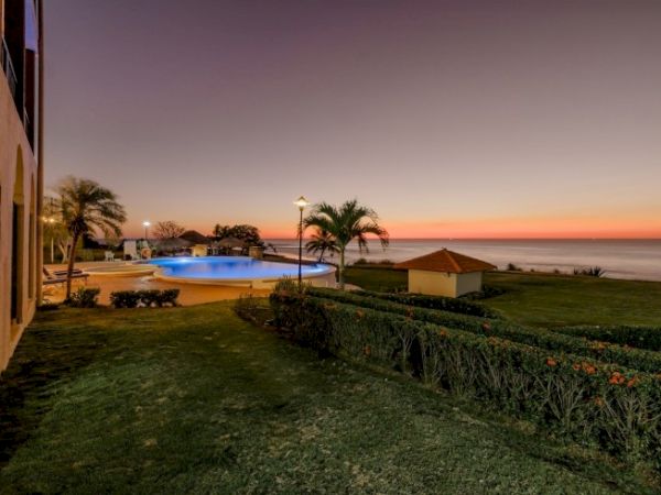 Sunset over a beachside property with a swimming pool, palm trees, and a grassy lawn.