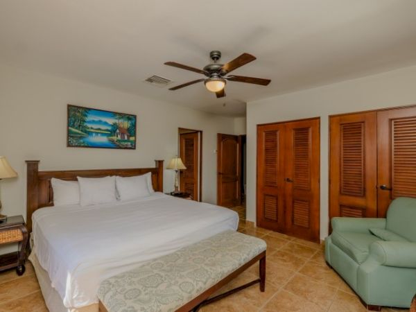 A bright bedroom with a bed, ceiling fan light, wooden doors/closet shutters, and a green sofa in the corner.