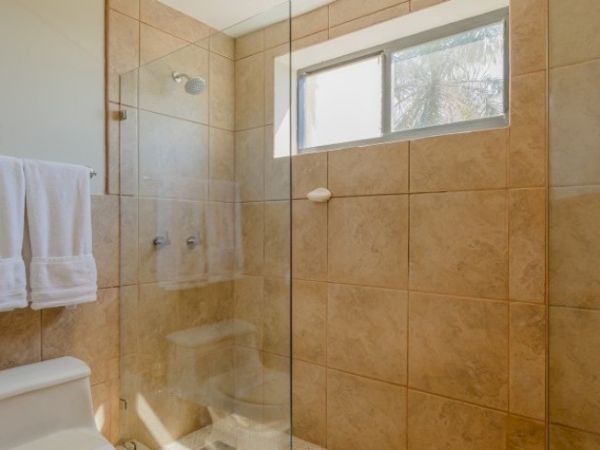 A tiled bathroom with a glass shower enclosure, a showerhead, and a window above the shower area.