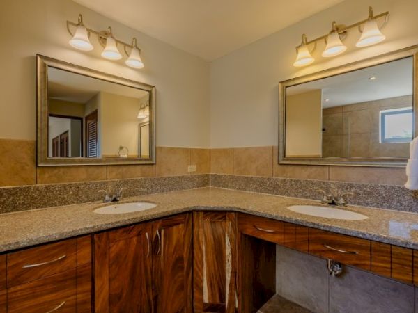 A bright bathroom with double vanity sinks, granite countertop, wall mirrors, and ceiling light fixtures.