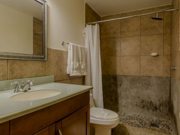 A tiled bathroom with a vanity sink, wall mirror, and walk-in shower with a curtain and handheld showerhead.