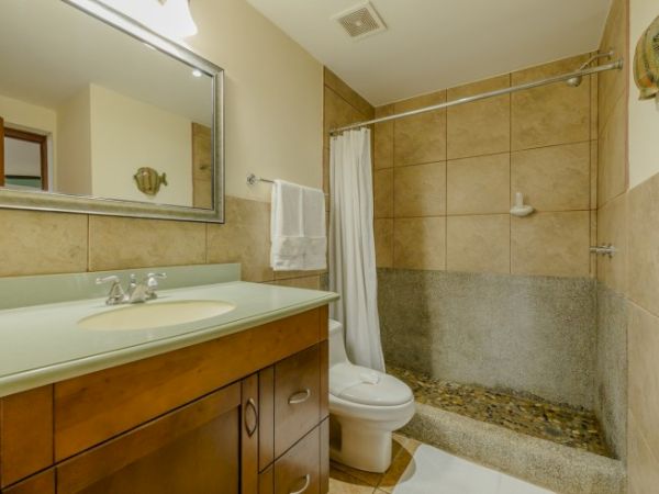 A small bathroom with a vanity sink, toilet, shower/tub combo, towel rack, and beige tile walls.