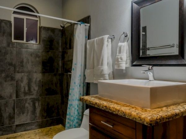 A modern bathroom with a granite countertop sink, mirror, towels, and a shower curtain by the tiled wall.