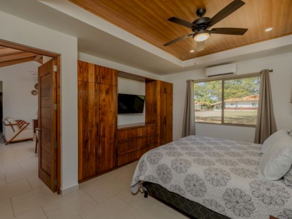 A cozy bedroom with a ceiling fan, bed, window view, and warm wood paneling walls.