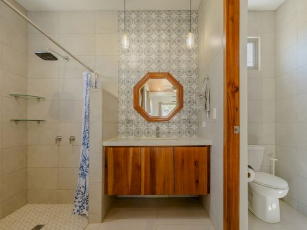 A bright modern bathroom with a tiled shower, wooden vanity, patterned wall, and a wall mirror above the sink.