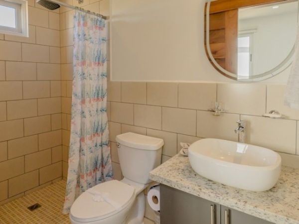 A modern bathroom with tiled walls, a toilet, a round sink, and a shower with a patterned curtain.