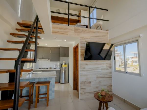 A modern open-plan apartment interior with a spiral staircase, kitchen, TV feature wall, and a bright window view.