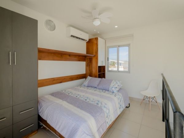 Bright modern bedroom with a bed, wood slat wall, gray wardrobe, ceiling fan, and a small chair by the window.
