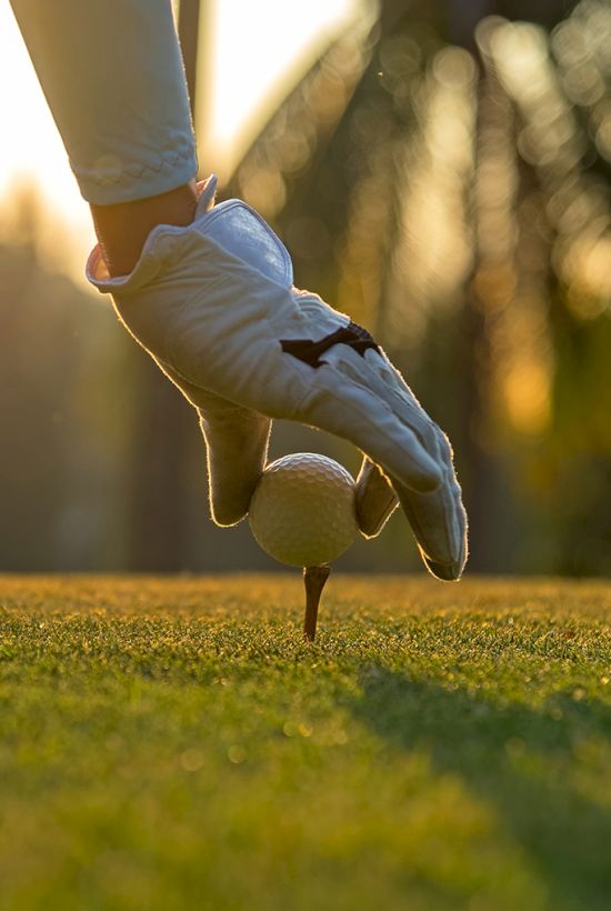 A child kicks a golf ball on a tee on a sunny grassy course.