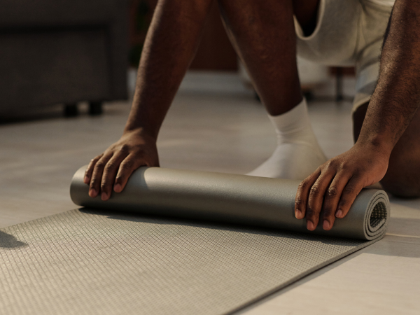 A person rolls out a yoga workout mat and smooths it on the floor with both hands.