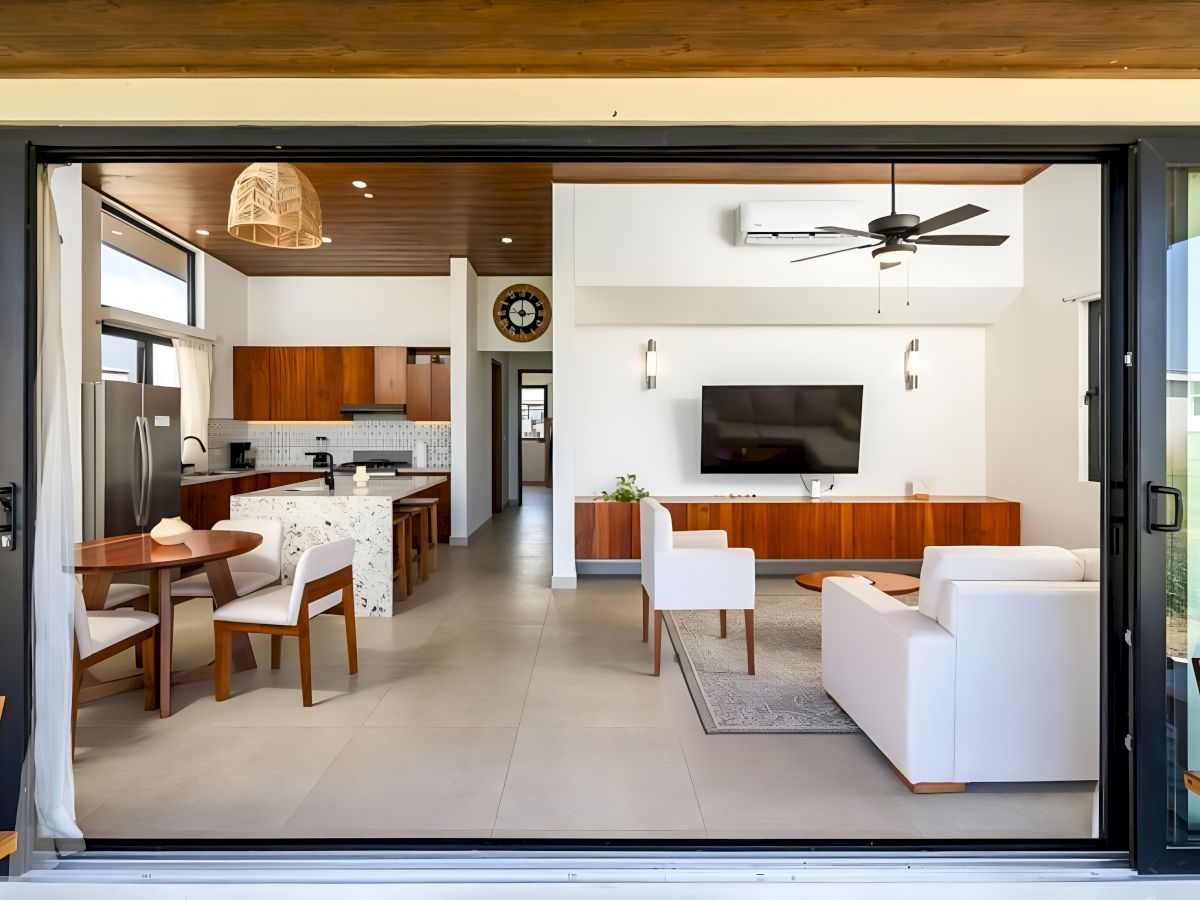 Modern open-plan living room and kitchen with white sofa, TV wall, ceiling fan, pendant lights, and marble island.