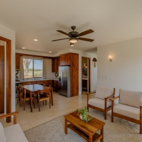 Bright open-concept living room and kitchen with tile floors, wooden cabinets, a dining set, and a ceiling fan overhead.
