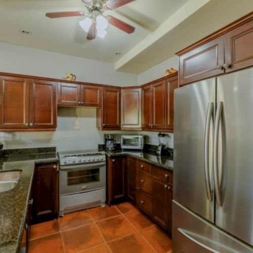 A bright kitchen with dark wood cabinets, granite counters, a stove/oven, refrigerator, sink area, and a ceiling fan.
