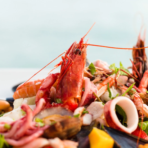 A close-up seafood platter with shrimp, mussels, clams, and herbs on a black plate.