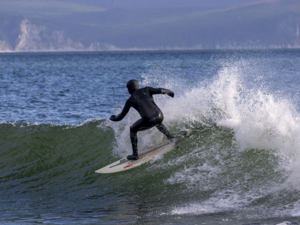 A surfer in a wetsuit carves a powerful wave, splashing spray under a cloudy sky.