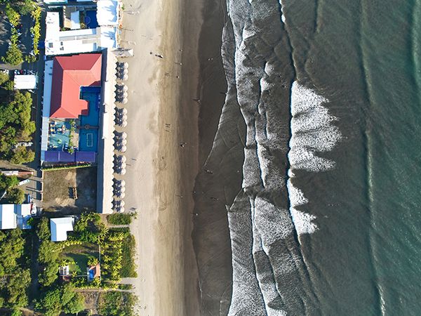 Aerial view of a beachfront resort with sandy shore and waves along a rocky coastline and docks.