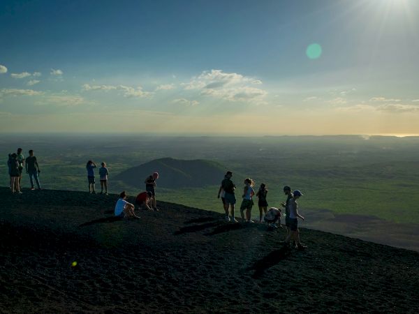 A group of hikers stands on a mountaintop at sunrise, looking out over rolling green valleys.