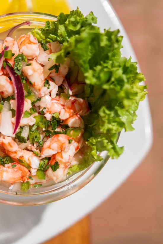 A glass bowl of shrimp salad with mixed greens, diced onions, herbs, and veggies.